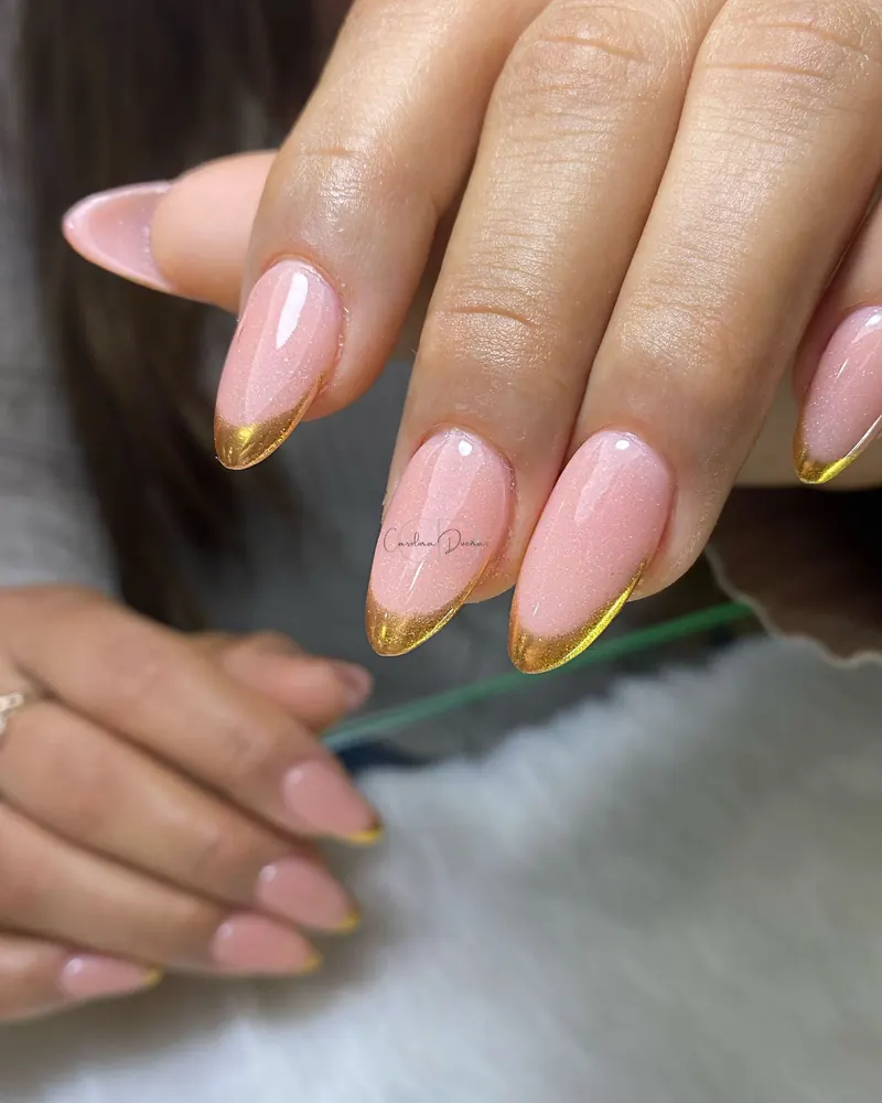 Manicura francesa con punta dorada sobre base rosa, uñas en forma de almendra